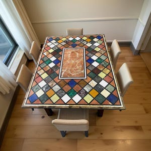 Puede incluir: Una mesa de comedor rectangular con una encimera de mosaico con una variedad de formas geométricas coloridas. La mesa está rodeada de seis sillas tapizadas beige. El panel central es de mármol marrón rojizo y el marco es de madera oscura.