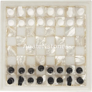 Könnte beinhalten: Ein weißes Marmorschachbrett mit schwarzen und weißen Figuren. Das Brett ist aus eingelegtem Perlmutt gefertigt und hat einen weißen Rand.