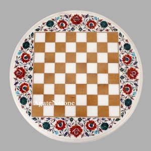 May include: Round marble chess board with a white base and a brown and white checkered playing surface. The border features a floral design with red, green, and blue accents. The text "AgateNstone" is visible on the board.