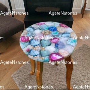 May include: A small, round side table with a unique agate top. The top is made of a variety of colors, including pink, blue, and white. The table has three legs and is made of wood.