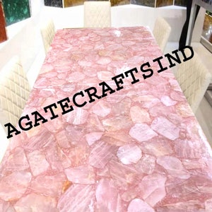 May include: A rectangular dining table with a pink, mosaic-like surface made of rose quartz. The table is surrounded by four cream-colored chairs. The text "AGATECRAFTSIND" is printed across the image.