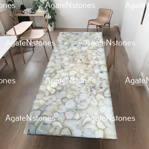 May include: A rectangular table with a surface made of white and beige agate stone slices. The table is in a room with wooden floors and light-colored chairs. The text "AgateNstones" is watermarked across the image.