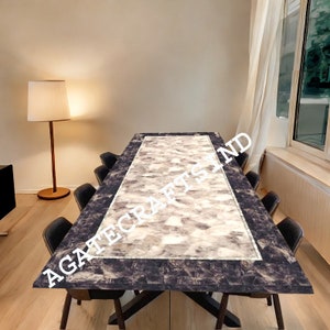 Può includere: Un grande tavolo da pranzo con un piano in pietra di agata bianco e grigio e un bordo nero. Il tavolo è circondato da sedie nere. Il testo "AGATE CRAFTS IND" è visibile sul piano del tavolo.