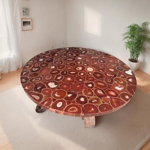 May include: A large, round coffee table with a mosaic top made of polished agate slices in shades of red, brown, and white. The table has a unique, natural stone pattern and is supported by a wooden base. The table is approximately 48 inches in diameter.