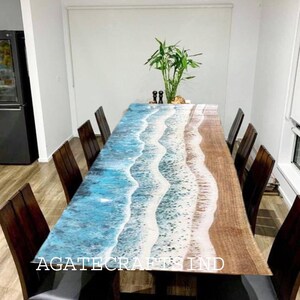 May include: A large wooden dining table with a resin ocean wave design. The table is surrounded by black chairs and has the text "AGATECRAFTS IND" on the surface.