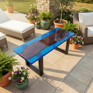 May include: A rectangular outdoor coffee table with a blue resin top and a dark wood inlay. The table has black metal legs and is surrounded by potted plants and patio furniture. The table measures approximately 48 inches long.