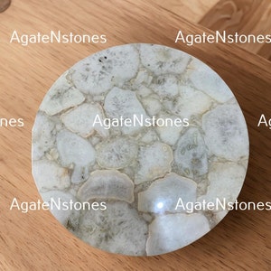 May include: A white agate coaster with a circular shape and a natural, organic pattern. The coaster is made of polished agate and has a smooth, glossy finish.