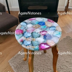 May include: A round side table with a unique agate stone top. The table has three legs and is made of wood. The agate stone top is a mix of blue, pink, white, and gray colors.