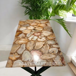 Könnte beinhalten: Ein Couchtisch mit einer einzigartigen Tischplatte aus Achat. Der Tisch hat ein schwarzes X-förmiges Gestell. Der Achat ist eine Mischung aus braunen, beige und weißen Farben. Der Tisch heißt "Agate Crafts Ind".