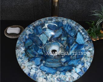 Pode incluir: Uma pia redonda de pedra de ágata azul e branca com ralo central. A pia é feita de pedaços de pedra azul e branca de formato irregular. O texto "AGATE CRAFTS IND" é visível. Uma torneira de bronze é visível.