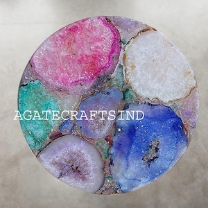 May include: A round decorative tabletop made of colorful agate slices. The agate pieces are in shades of pink, blue, green, and white, arranged in a mosaic pattern. The text "AGATECRAFTSIND" is printed on the surface.