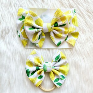May include: Two lemon-print hair bows, one large and one small. The large bow is attached to a white headband, while the small bow is attached to a nude elastic.