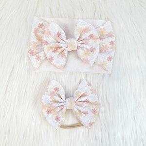 May include: Two floral print hair bows, one large and one small. The larger bow is attached to a nude headband, while the smaller bow is attached to a nude elastic headband.