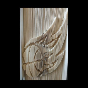 Puede incluir: Primer plano de una escultura de arte de libro, hecha doblando las páginas de un libro para crear un diseño 3D. La escultura tiene forma de ala, con un patrón detallado e intrincado.