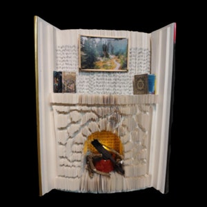 Puede incluir: Una chimenea hecha de las páginas de un libro, con una pequeña imagen de una escena de bosque encima. La chimenea tiene una pequeña luz en su interior, y hay libros en la estantería de arriba.