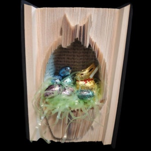 May include: A book with pages folded into the shape of a bunny rabbit, holding chocolate eggs and a chocolate bunny. The book is open and the bunny is visible in the center of the book.