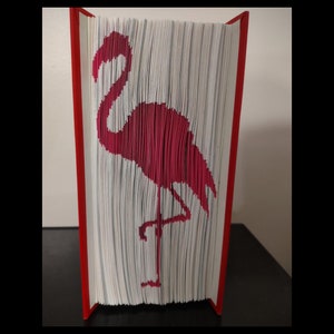Op de afbeelding: Een boek met een rode kaft is gevouwen om een ​​3D origami-achtig beeld van een roze flamingo te creëren.