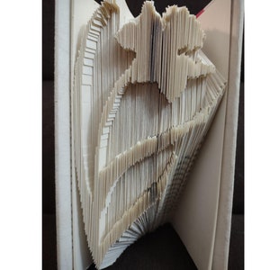Op de afbeelding: Een handgemaakte boekkunstsculptuur met een bloemmotief. De pagina's zijn zorgvuldig gevouwen en gesneden om een driedimensionale bloemvorm te creëren. Het boek is open en toont de ingewikkelde details van het papierambacht.