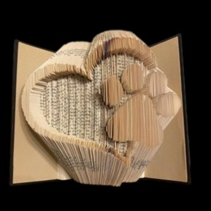 Peut inclure: Une sculpture d'art de livre en forme de cœur avec une empreinte de patte à l'intérieur. La sculpture est réalisée à partir des pages d'un livre qui ont été pliées et façonnées pour créer le design. La sculpture est de couleur brun clair.