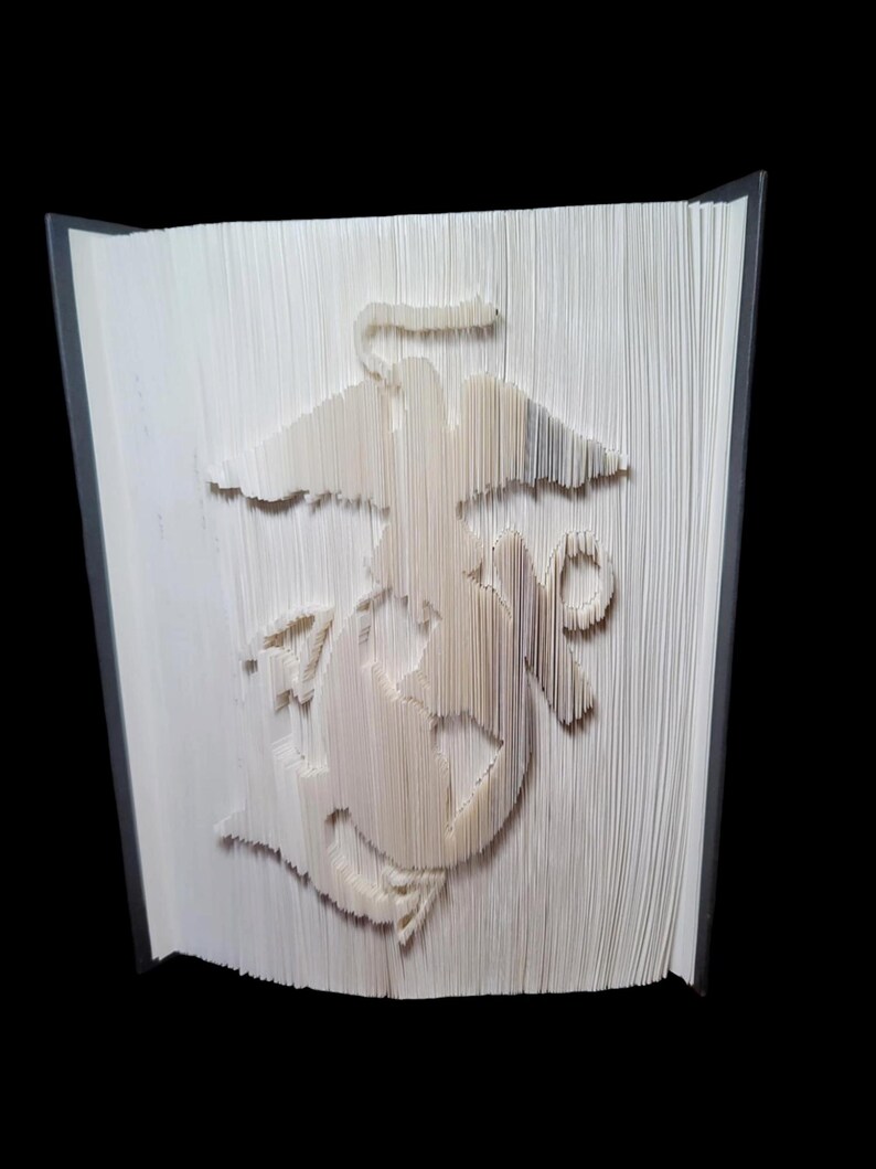 Puede incluir: Un libro blanco con el emblema del Cuerpo de Marines doblado en las p&aacute;ginas. El emblema es un &aacute;guila estilizada, un globo terr&aacute;queo y un ancla.