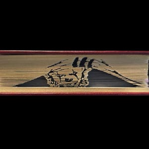 May include: A book with a red cover has been cut and folded to create a detailed silhouette of a bear's head. The bear's head is facing the viewer and is partially obscured by the book's pages.