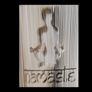 Könnte beinhalten: Eine Buchkunstskulptur einer stehenden Person mit dem Wort "Frieden" gefaltet in den Boden der Skulptur.