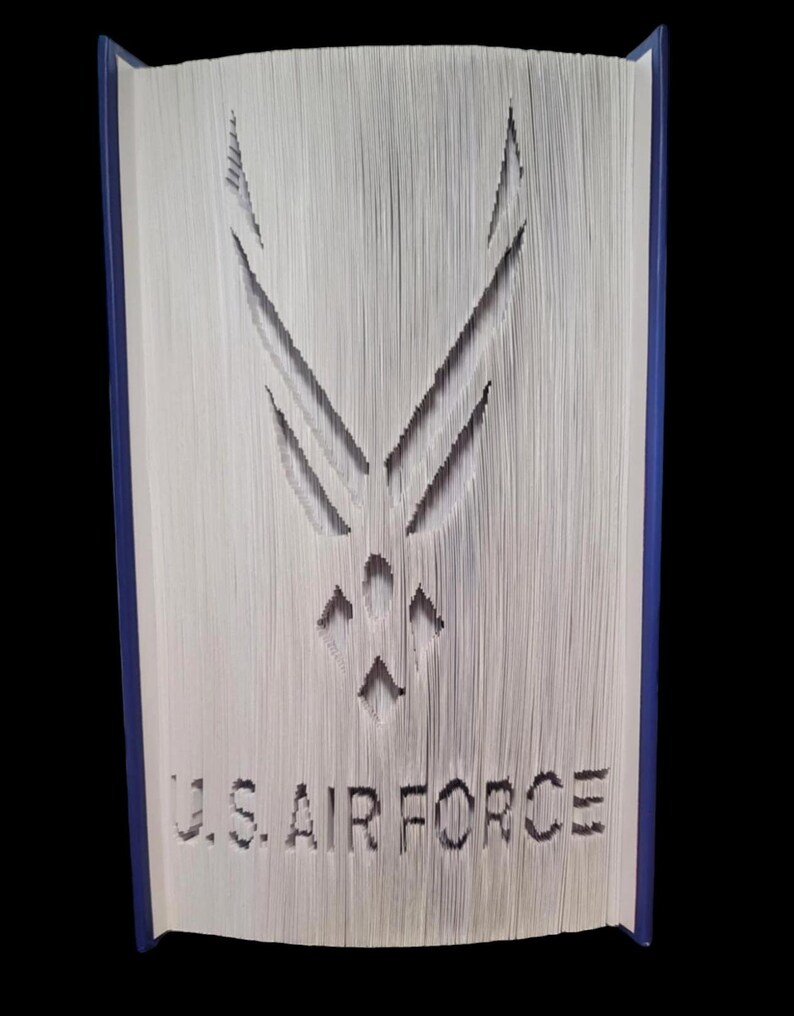 Puede incluir: Un libro con el logotipo de la Fuerza A&eacute;rea de los Estados Unidos recortado en las p&aacute;ginas. El logotipo es una estrella estilizada con alas. Las palabras "U.S. AIR FORCE" est&aacute;n recortadas debajo del logotipo.