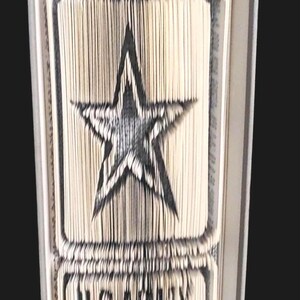 Puede incluir: Un libro doblado en forma de estrella de cinco puntas con las palabras "U.S. ARMY" debajo.