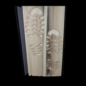 May include: A book with the pages folded to create a 3D image of two footprints. The footprints are made from the pages of the book.