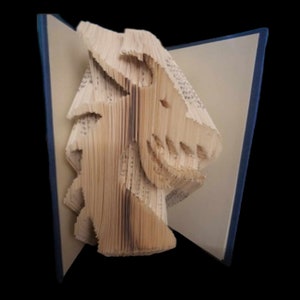 May include: A book sculpture of a dragon's head, made from the pages of a book. The sculpture is standing upright on a table. The book is bound in blue and has a white cover.