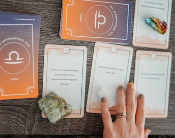Pode incluir: Um conjunto de cartas de afirmação para o signo do zodíaco Libra. As cartas são cor de pêssego e laranja com um símbolo de Libra e o texto "100 Afirmações para Libra". Um cartão tem a afirmação "Embora eu seja habilidoso em trazer paz aos outros, devo lembrar de também trazer paz para mim mesmo."