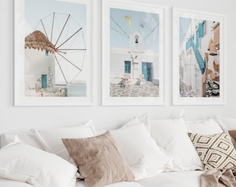 May include: Three framed wall art prints featuring Greek island architecture. The left print shows a traditional windmill, the center print displays a white building with blue doors, and the right print depicts a narrow street with blue stairs and decor.