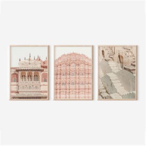 May include: Set of three framed prints featuring architectural images. The prints showcase buildings with intricate details and a soft color palette of pinks, creams, and grays. The frames are a light wood color.
