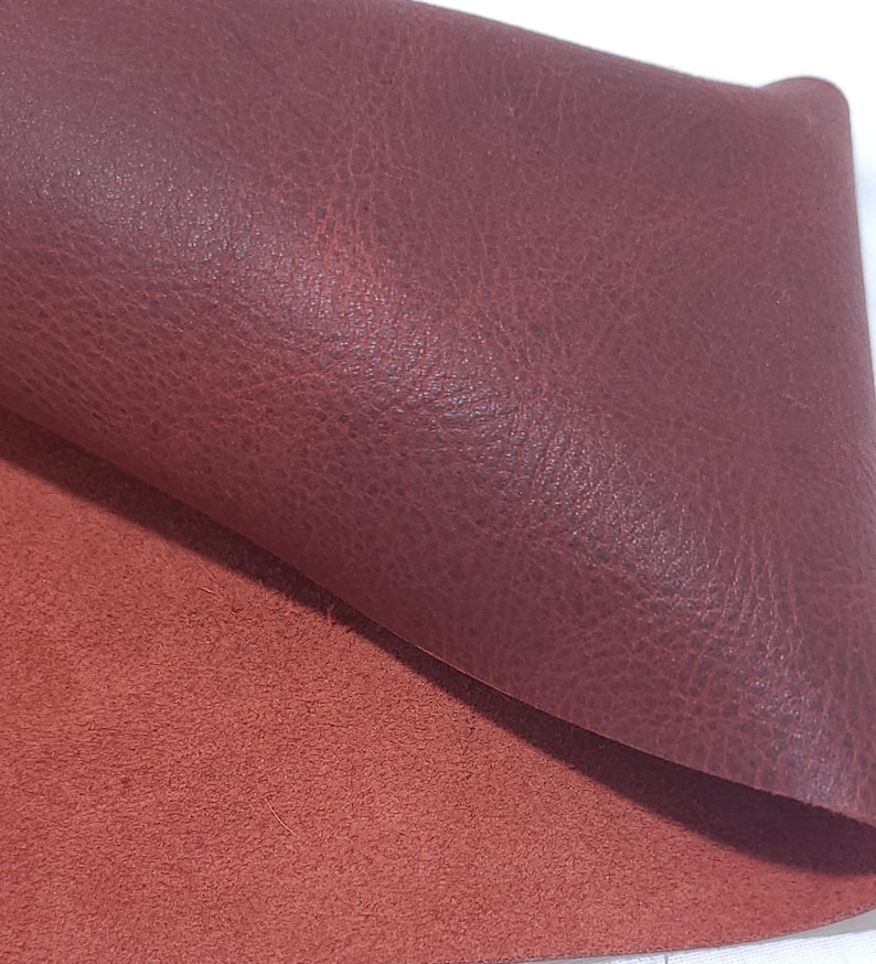 Pu&ograve; includere: Primo piano di due pezzi di pelle bordeaux. Il pezzo superiore &egrave; ripiegato, rivelando una superficie strutturata. Il pezzo inferiore &egrave; di una tonalit&agrave; di rosso pi&ugrave; chiara, con una texture simile alla pelle scamosciata. La pelle viene probabilmente utilizzata per l'artigianato.