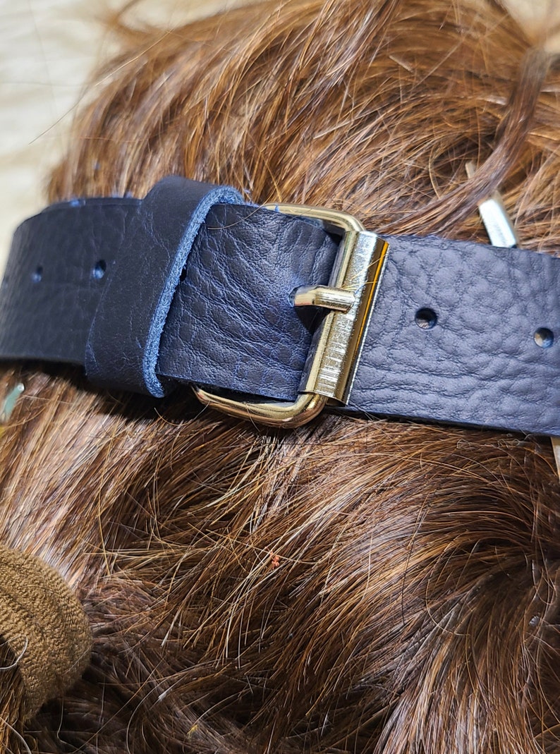 Pu&ograve; includere: Primo piano di una cintura in pelle blu navy con fibbia color argento. La cintura ha una superficie strutturata ed &egrave; fissata con una fibbia in metallo. La cintura &egrave; probabilmente per l'abbigliamento.