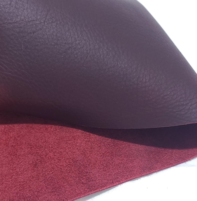 Pu&ograve; includere: Primo piano di un pezzo di pelle bordeaux, che rivela una superficie superiore strutturata e un lato inferiore rosso a contrasto e pi&ugrave; morbido. La pelle &egrave; piegata, mostrando le diverse trame e colori.