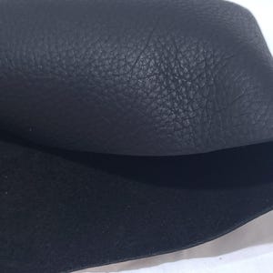 Pu&ograve; includere: Primo piano di pelle nera con superficie strutturata. La pelle &egrave; ripiegata, rivelando un lato inferiore liscio e contrastante. L'immagine evidenzia la grana e il colore del materiale.