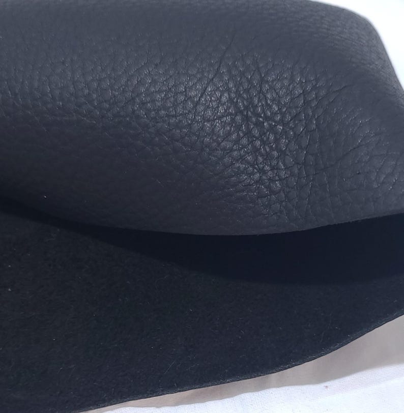 Pu&ograve; includere: Primo piano di pelle nera con superficie strutturata. La pelle &egrave; ripiegata, rivelando un lato inferiore liscio e contrastante. L'immagine evidenzia la grana e il colore del materiale.