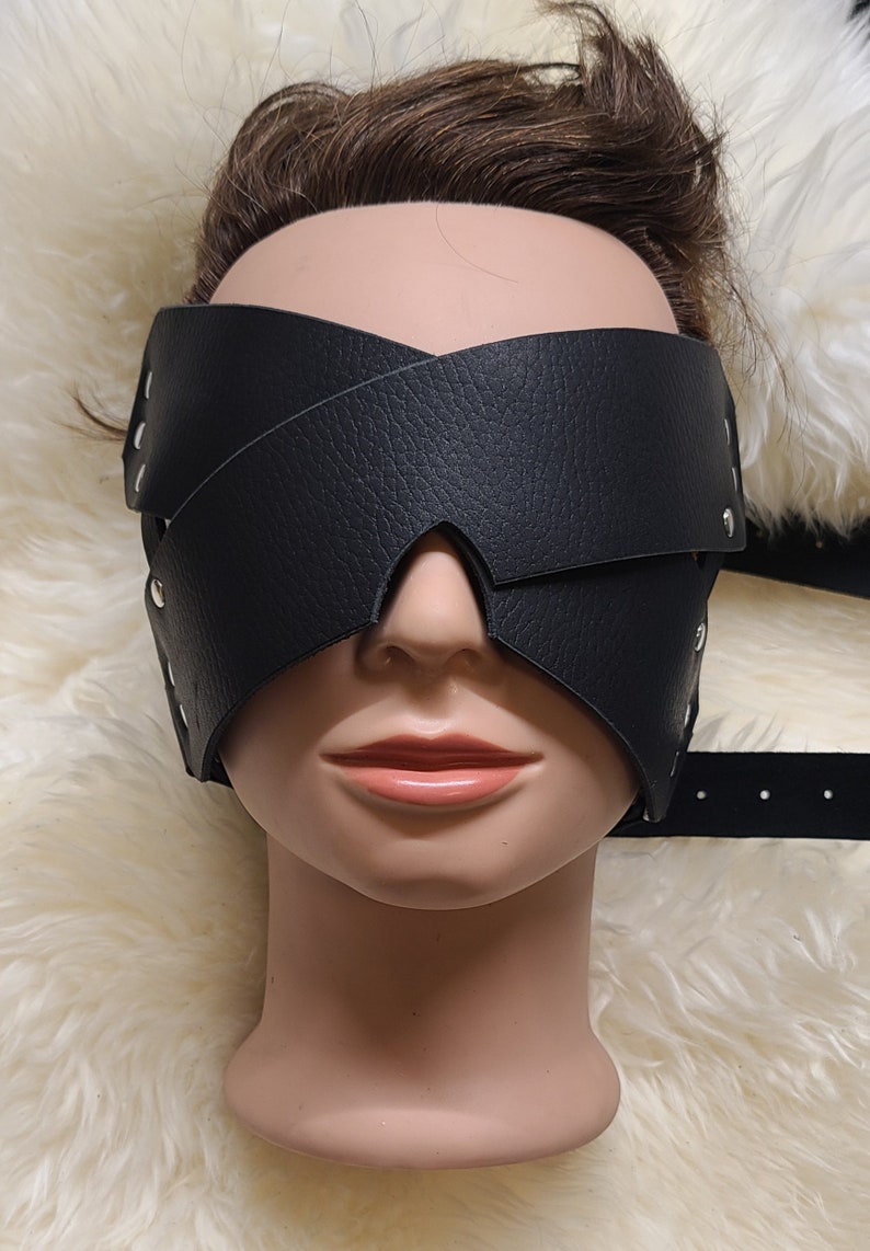 Pu&ograve; includere: Benda per gli occhi in pelle nera con un design a croce, fissata con rivetti color argento. La maschera copre gli occhi ed &egrave; progettata per la deprivazione sensoriale. Il prodotto &egrave; esposto su una testa di manichino.
