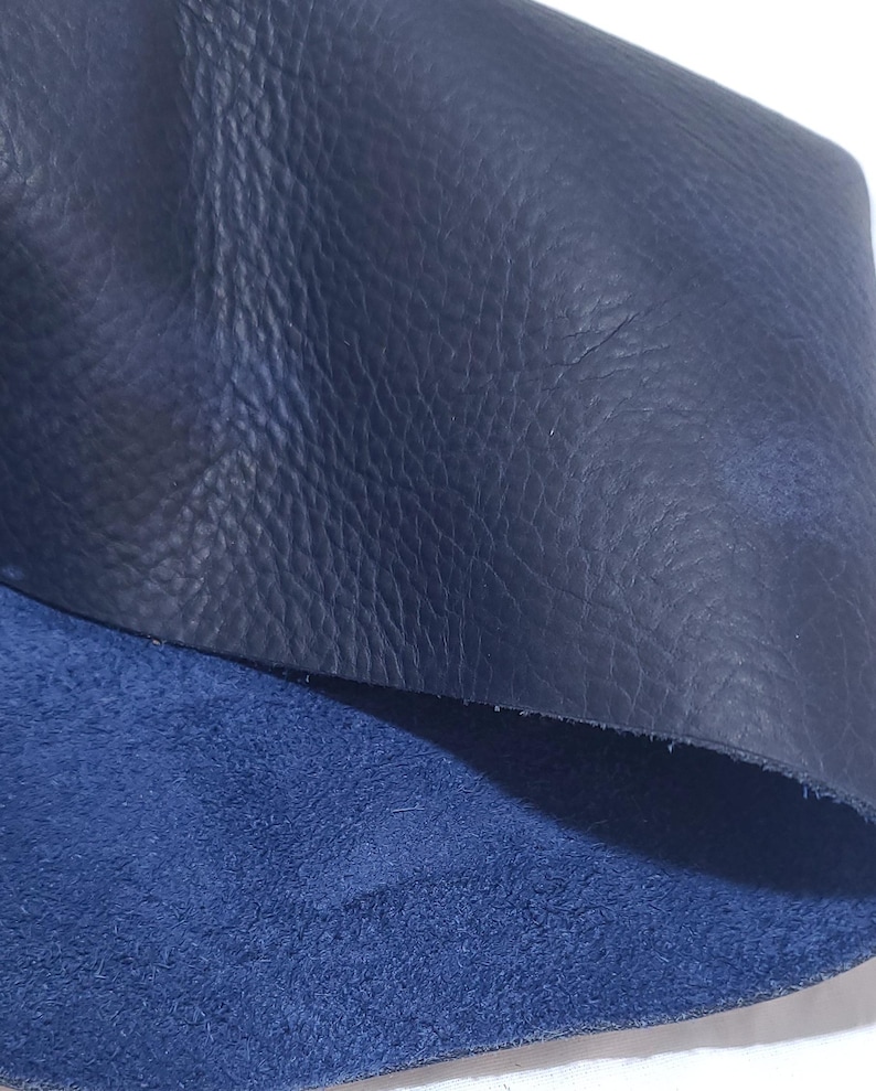 Pu&ograve; includere: Primo piano di due pezzi di pelle blu navy. Il pezzo superiore ha una superficie strutturata e granulosa, mentre il pezzo inferiore ha una consistenza pi&ugrave; morbida, simile alla pelle scamosciata. La pelle &egrave; di una tonalit&agrave; blu profonda e ricca.