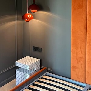 May include: A bedroom with a bed, a bedside table, and three red pendant lights hanging from the ceiling. The wall behind the bed is a burnt orange color.