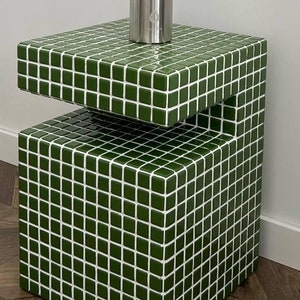 May include: A stainless steel water bottle with a carrying handle sits on a green tiled table. The table has a unique design with a cut-out section. The text on the image reads "SKARBI @USUALONE_BOTTLE #TILECUBESTUDIO".