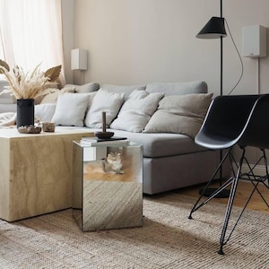 May include: A light gray sofa with multiple pillows sits in a living room with a black floor lamp, a black chair, and a wooden coffee table with a mirrored side table.