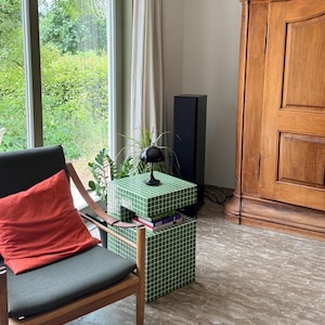 Könnte beinhalten: Ein Wohnzimmer mit einem grünen, gefliesten Beistelltisch und einer schwarzen Lampe. Ein orangefarbenes Kissen liegt auf einem dunkelgrauen Stuhl. Ein großer Holzschrank und ein hoher schwarzer Lautsprecher sind ebenfalls zu sehen. Der Tisch ist etwa 40 cm hoch.