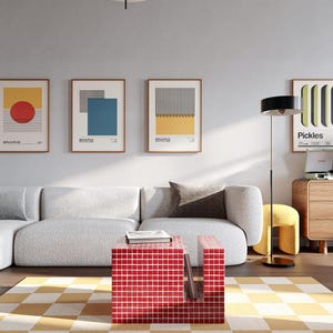 Puede incluir: Un salón moderno con un sofá blanco, una mesa de centro roja con azulejos y una alfombra a cuadros amarillos y blancos. Tres estampados enmarcados de estilo Bauhaus cuelgan de la pared. Una lámpara de pie negra y un pequeño taburete amarillo completan la decoración.
