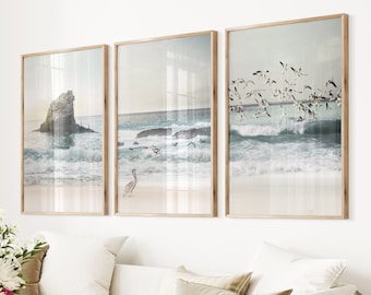 May include: Three framed prints of seascapes with a beach, ocean waves, and birds flying overhead. The prints are in wooden frames with a light wood finish.