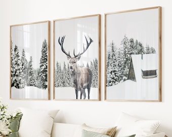May include: Three framed prints of a winter scene with a red deer standing in a snowy forest. The middle print features the deer in the foreground, while the other two prints show a snowy forest with a cabin in the distance.
