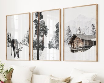 May include: Three framed art prints showcasing winter landscapes. The prints display a deer in a snowy forest, a snow-covered path through trees, and a wooden cabin in a snowy mountain setting. The frames are made of light-coloured wood.