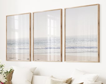 May include: Three framed prints of a beach scene with blue water and white waves crashing on the shore. The prints are in wooden frames and are hung on a white wall.