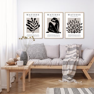 May include: Three black and white art prints with the text "MATISSE" and "BERGRUEN & CIE" in a beige frame. The prints feature abstract designs of a plant, a woman, and a cluster of leaves.